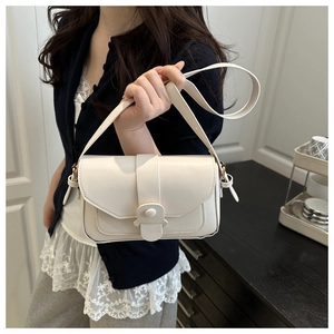 Detail of cream flap crossbody bag with semi-circle snap closure worn by model