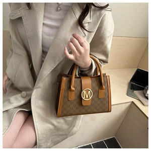 Close-up of brown monogram tote bag with gold M-logo buckle on a beige coat background