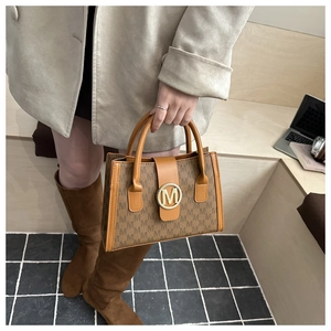 Detail of brown monogram tote bag with golden metal logo and premium leather texture