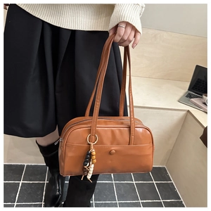 Close-up of a brown leather bowling bag with retro bead charm and front pocket detail