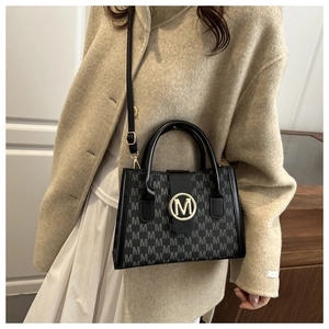 Detail of black monogram shoulder bag with gold M logo on a model's beige coat