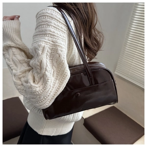 Detailed view of the dark brown glossy leather shoulder bag worn over a white sweater