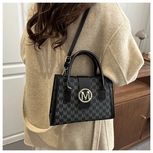 Detail view of a black chic crossbody bag with M-pattern on a woman in a beige coat