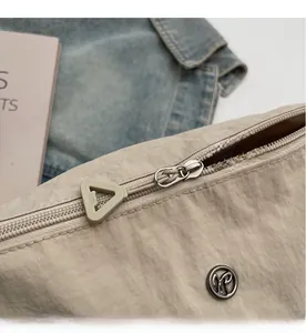 Close-up of smooth metal zipper and triangle puller on beige nylon dumpling bag