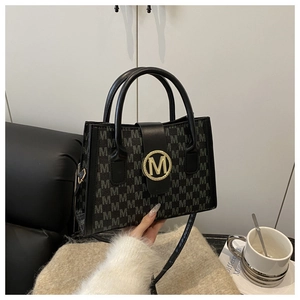 Detailed view of black tote bag with gray M-monogram and large gold buckle