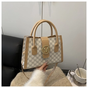 Detail of a chic tote bag with monogram texture and golden metal M-shaped buckle