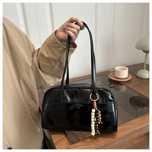 Detail of black glossy handbag with stylish tricolor beaded charm on wooden cabinet