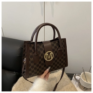 Detailed close-up of dark brown leather tote bag with M-pattern print and gold clasp