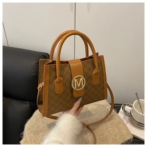 Detail of brown monogram shoulder bag featuring a prominent gold M-shaped circular buckle