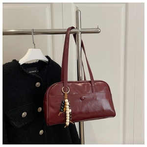 Close-up of a glossy burgundy faux leather bowling bag with a colorful beaded pendant