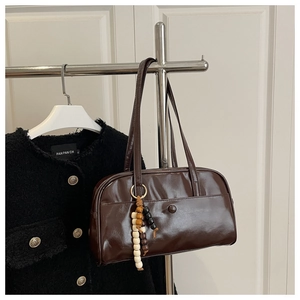 Detail of dark brown glossy leather bowling bag with vintage beaded charm on a metal hanger