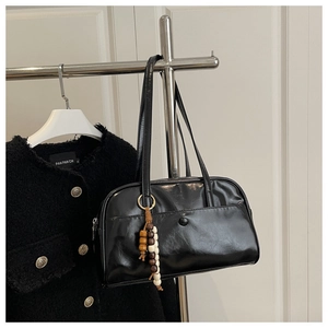 Detailed macro view of black glossy leather bag with wooden bead fringe pendant