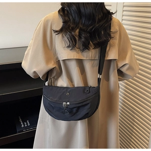 Close-up of black crescent nylon crossbody bag worn with a classic khaki trench coat