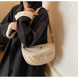 Side view of a beige nylon dumpling bag with adjustable strap worn by a model