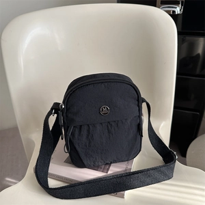 Black lightweight nylon crossbody bag with wide strap on a minimalist white chair