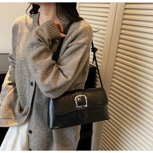 Close-up of black leather baguette bag with silver buckle and knotted strap detail