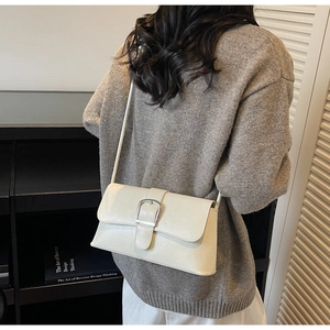 Close-up of a white French baguette bag featuring a polished silver buckle on shiny PU leather