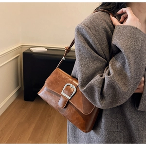 Detail of vintage brown oil wax leather baguette bag with a silver buckle on a grey blazer