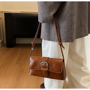Close-up of brown vintage leather baguette bag with silver horseshoe buckle and knotted strap