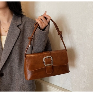 Close-up of retro brown shoulder bag featuring a large silver buckle and knotted strap