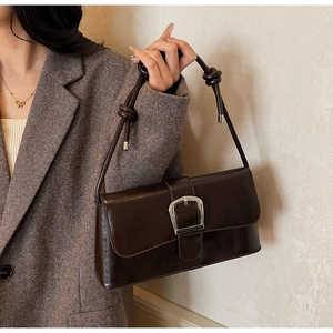 Detail of dark brown baguette bag with silver metal buckle and knotted shoulder strap