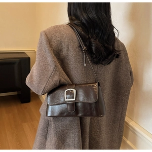 Dark brown patent leather baguette bag with silver metallic buckle on a grey tweed blazer