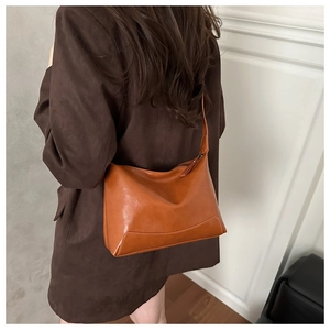 Caramel brown hobo tote bag worn with a dark brown blazer in a minimalist indoor setting