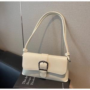 Detail of a white baguette bag featuring a silver buckle and knotted shoulder strap