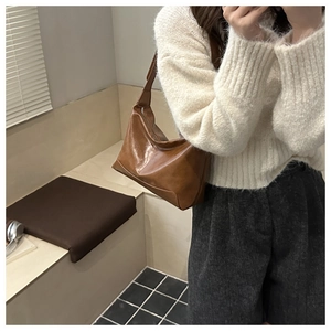 Close-up of a brown retro tote bag worn by a model in a minimalist indoor setting