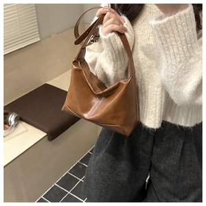 Detail of brown leather hobo bag with adjustable strap worn by model in warm lighting