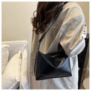 Detailed side view of a minimalist black tote bag worn by a model in a modern interior