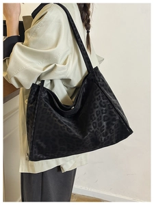 Close-up of a large black tote bag with a subtle leopard pattern on soft fabric texture