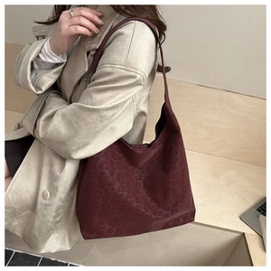 Detail view of burgundy tote bag with subtle leopard pattern worn by a model