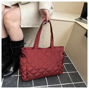 Detailed shot of burgundy quilted nylon tote bag with golden zipper and side pocket