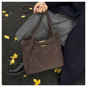 Detail of dark brown suede tote bag with woven handles and yellow text branding