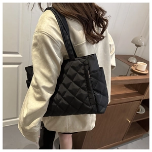 Detail of black quilted tote bag with side zipper pocket shown in lifestyle setting