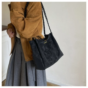Detail view of black faux suede tote bag featuring braided straps and gold brand logo