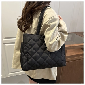 Rear view of a large black quilted tote bag with diamond pattern on a female model