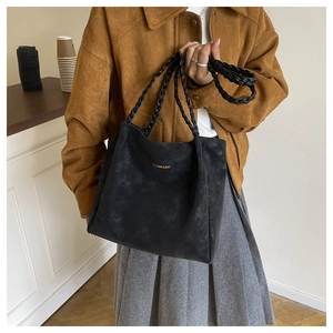 Close-up of black suede tote bag with woven leather handles and gold logo text