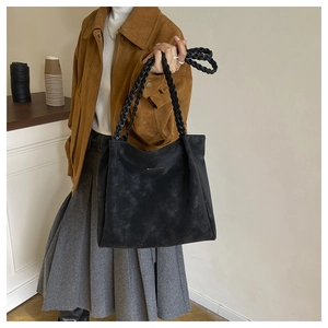 Detail of a black suede tote bag featuring a chunky braided handle and vintage texture