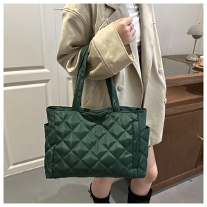 Detail of dark green quilted tote bag with side pocket held by model in indoor setting