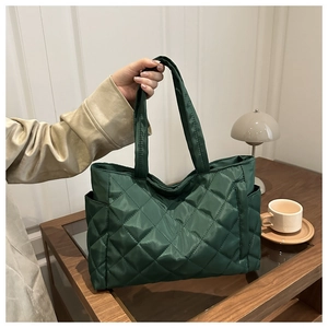 Close-up of dark green quilted tote bag featuring a diamond pattern and side pocket