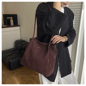 Detail of burgundy faux suede tote bag featuring a woven shoulder strap and gold logo