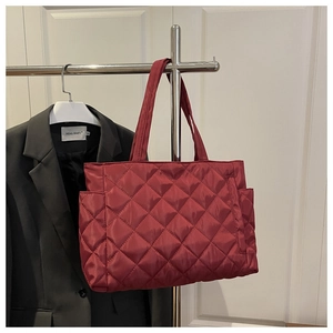 Detail of burgundy quilted tote bag with diamond pattern and side pocket on a hanger
