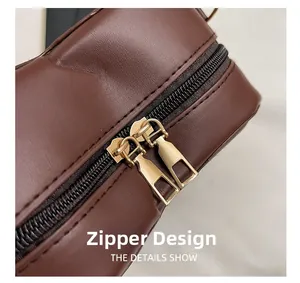 Detailed close-up of premium gold-toned dual zippers on a brown leather shoulder bag