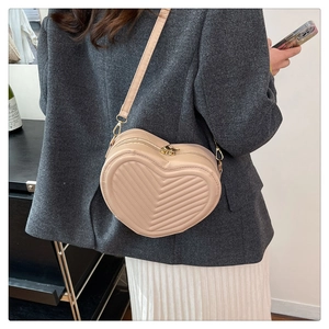 Close-up of beige heart-shaped crossbody bag with V-quilt pattern on grey suit