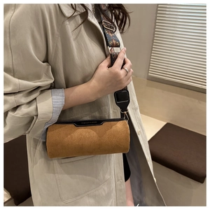 Detail of a brown suede cylinder bag with patterned strap on a beige trench coat