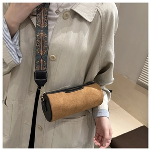 Close-up of brown suede cylinder bag with vintage patterned wide strap and black trim