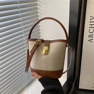 Chic cream canvas and brown leather bucket bag with a gold clasp on a minimalist background