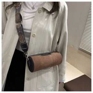 Detail view of brown frosted cylinder bag with ethnic patterned wide strap on a beige coat